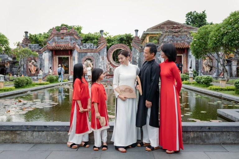 A family wearing traditional Ao Dai dresses poses by a pond at a temple in Hoi An, Vietnam.