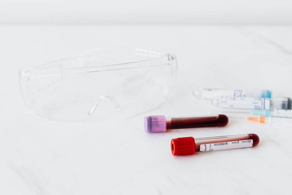 Close-up of medical vials with blood samples and protective eyewear on white background.