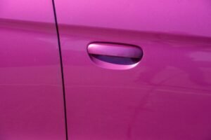 Close-up photograph of a vibrant pink car door handle, showcasing modern car design.