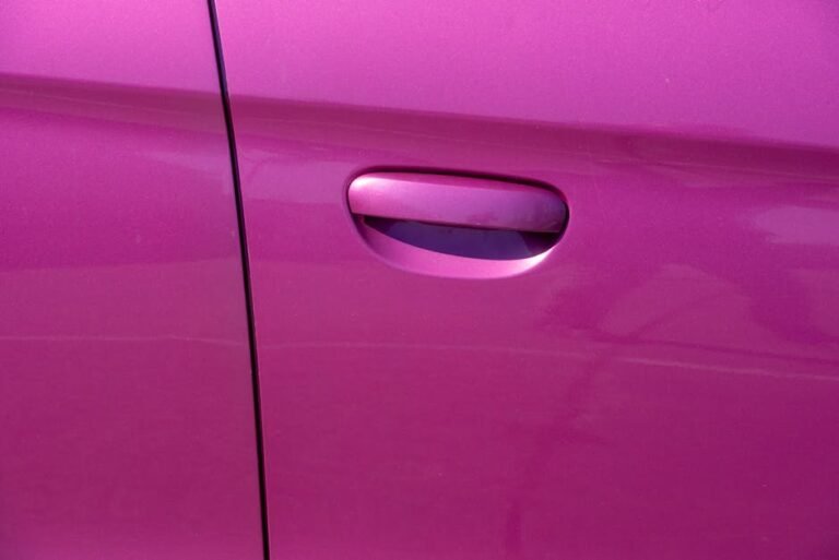 Close-up photograph of a vibrant pink car door handle, showcasing modern car design.