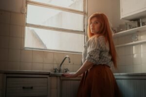 A woman stands thoughtfully in a sunlit kitchen in Buenos Aires, evoking warmth and reflection.