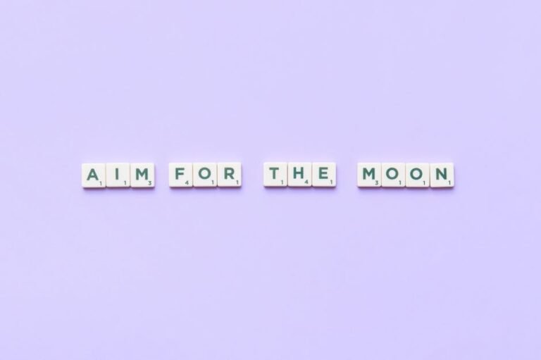 Scrabble tiles forming 'Aim for the Moon' on a purple background inspire motivation.