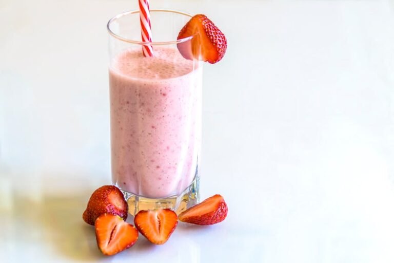Delicious strawberry smoothie in a glass with fresh strawberries and a striped straw on a light background.