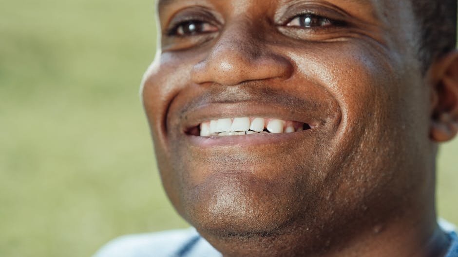 A close-up shot of a smiling black man outdoors with a focus on his cheerful expression and white teeth.