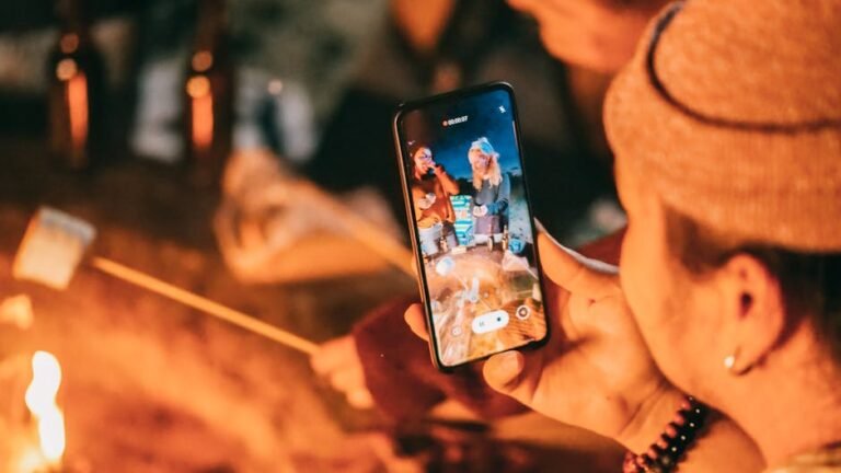 A group enjoys a night campfire, roasting marshmallows and recording with a smartphone.