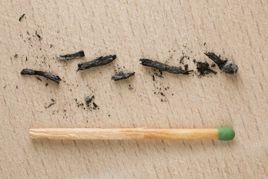 Close-up of a burnt matchstick and ash residue on a wooden surface, symbolizing ignition and burnout.