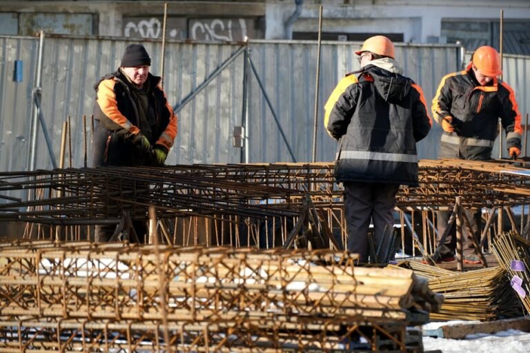 A group of construction workers managing steel rebar outdoors on a sunny day, wearing hard hats and safety jackets.