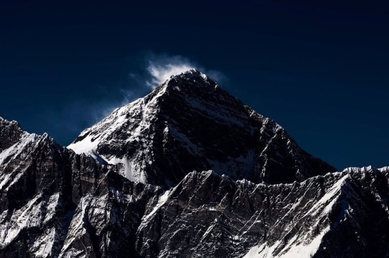 A stunning view of a snow-capped mountain peak with dramatic shadows under a dark sky.