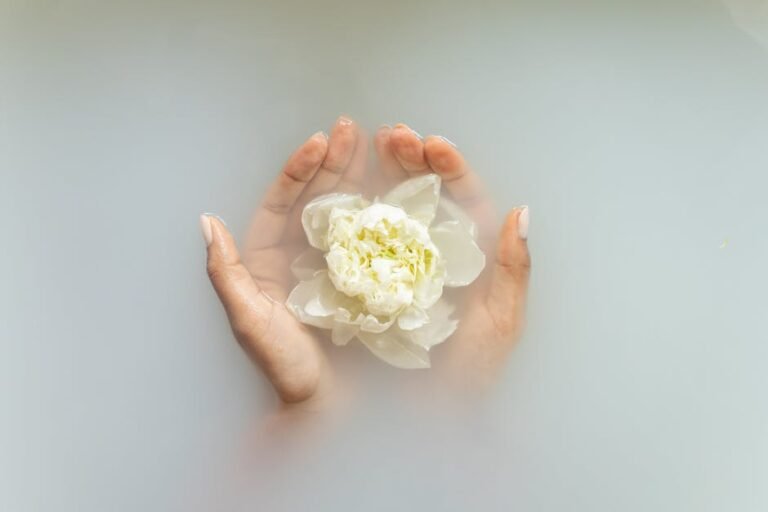 Hands holding a white flower in serene milky water, perfect for spa and wellness themes.