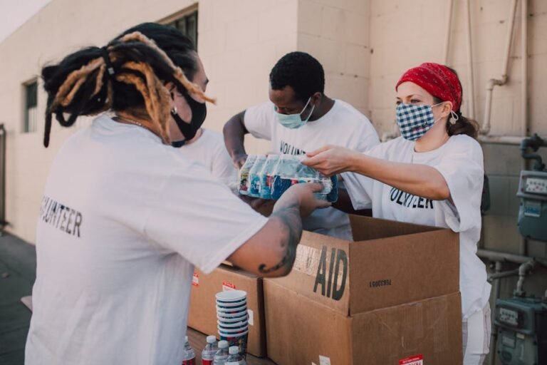 Volunteers wearing masks distribute aid boxes and water to the community outdoors.