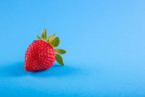 Vibrant close-up of a ripe strawberry on a blue backdrop, showcasing freshness.