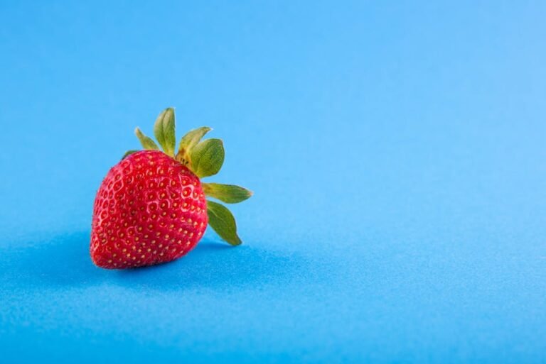 Vibrant close-up of a ripe strawberry on a blue backdrop, showcasing freshness.